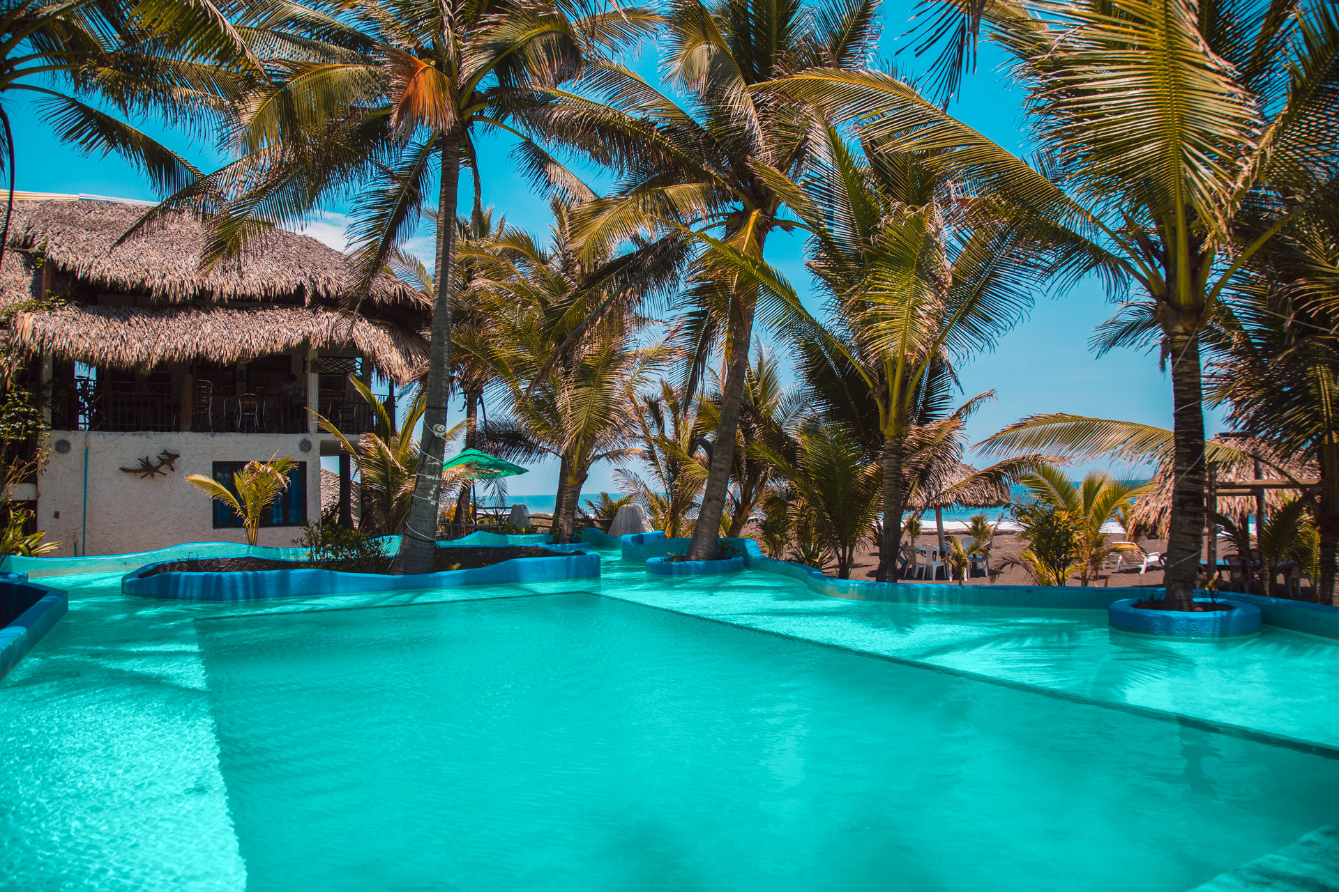 Piscina turquesa rodeada de palmeras bajo el cielo tropical de Monterrico