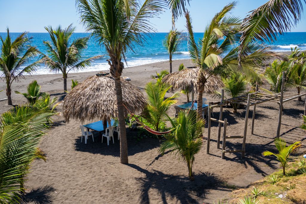 Playa de arena volcánica con ranchos de palma y hamacas